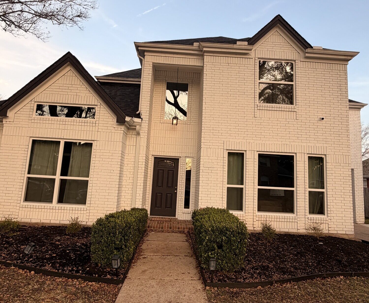Exterior view of the front of a two story white brick home with vinyl windows installed.