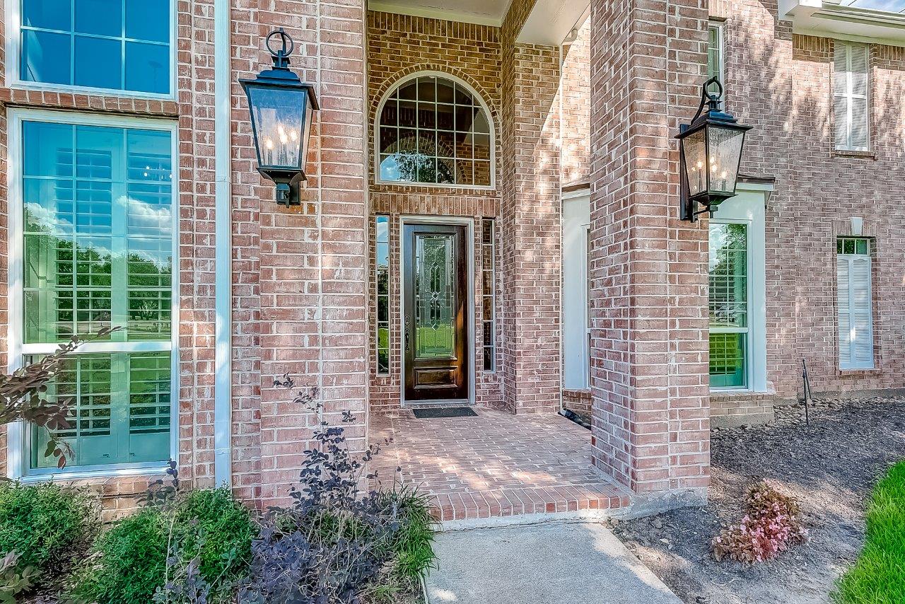 Exterior view of a large red brick home's entryway with vinyl windows and door installed.