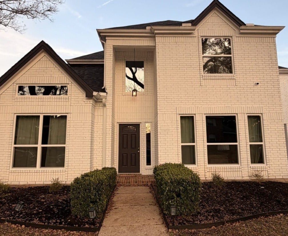 Exterior view of the front of a two story white brick home with vinyl windows installed.