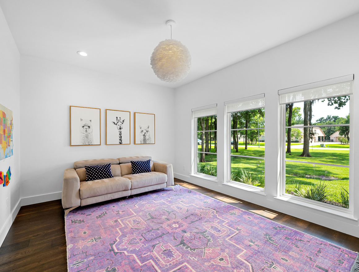 Bright living room with beige sofa, purple patterned rug, and three framed animal prints on white walls by large windows.