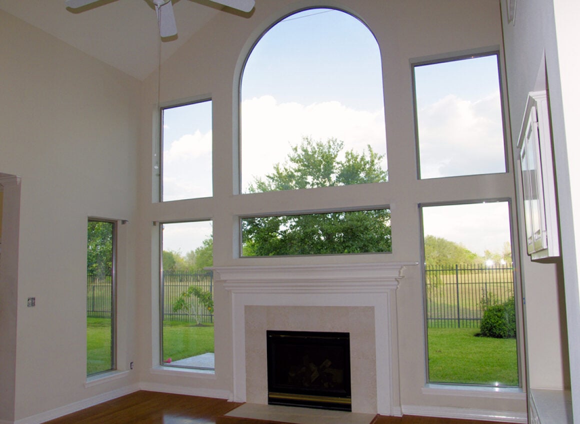 Bright living room with a white fireplace centered under a tall arched window flanked by rectangular windows, overlooking a green yard.