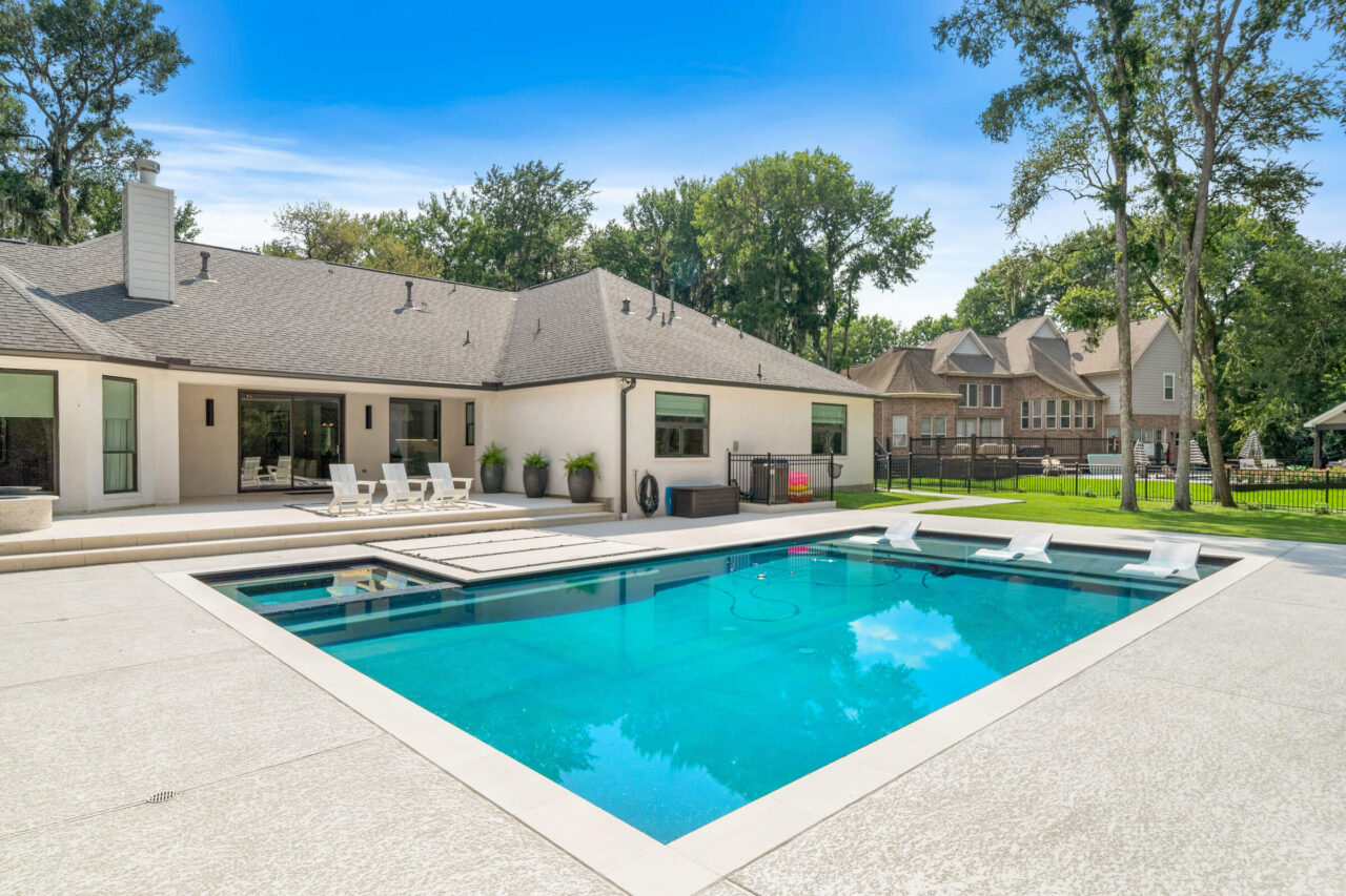 Best Time of Year to Buy Replacement Windows Backyard with a rectangular blue pool, white modern house, and patio chairs under a bright blue sky.